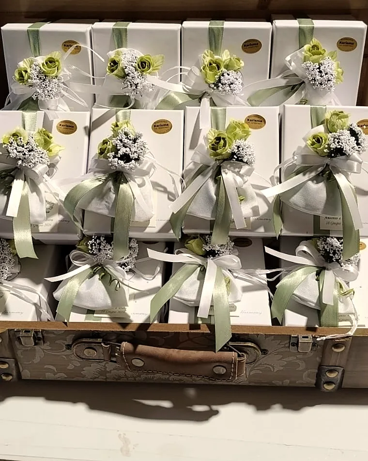 Valigia d'epoca piena di bomboniere Karisma: scatoline bianche con fiocchi salvia e mazzolini di fiori